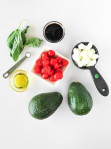 Caprese Stuffed Avocado ingredients sitting on a white surface.