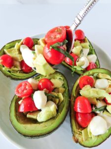 Stuffing avocado halves with Caprese Stuffed Avocado filling.