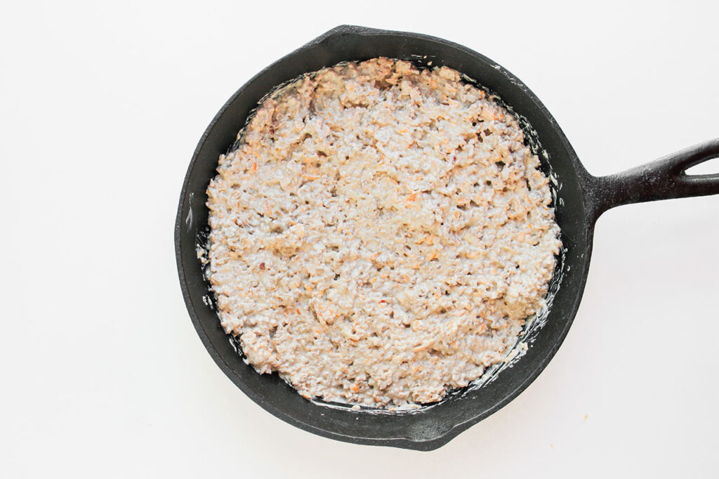 Meat mixture spread over the bottom of a cast iron skillet.