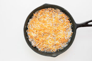 Shredded cheese sprinkled over the top of ground meat and cream cheese mix in a cast iron skillet.