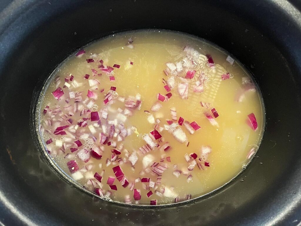 Chicken, onions, and broth in a slow cooker crock.