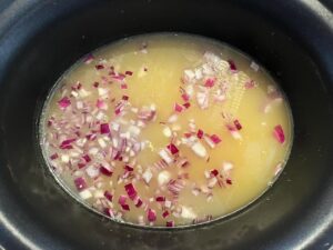 Chicken, onions, and broth in a slow cooker crock.