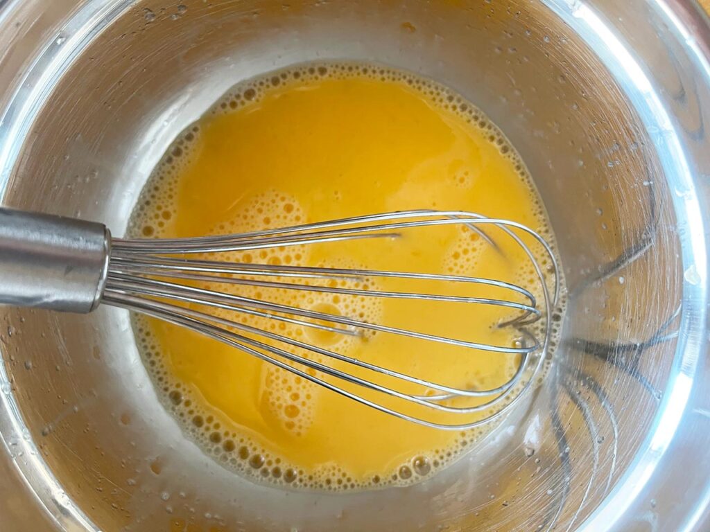 Whisked lemon and egg sauce for Greek Avgolemono Soup in a mixing bowl with a whisk.