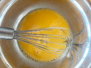 Whisked lemon and egg sauce for Greek Avgolemono Soup in a mixing bowl with a whisk.