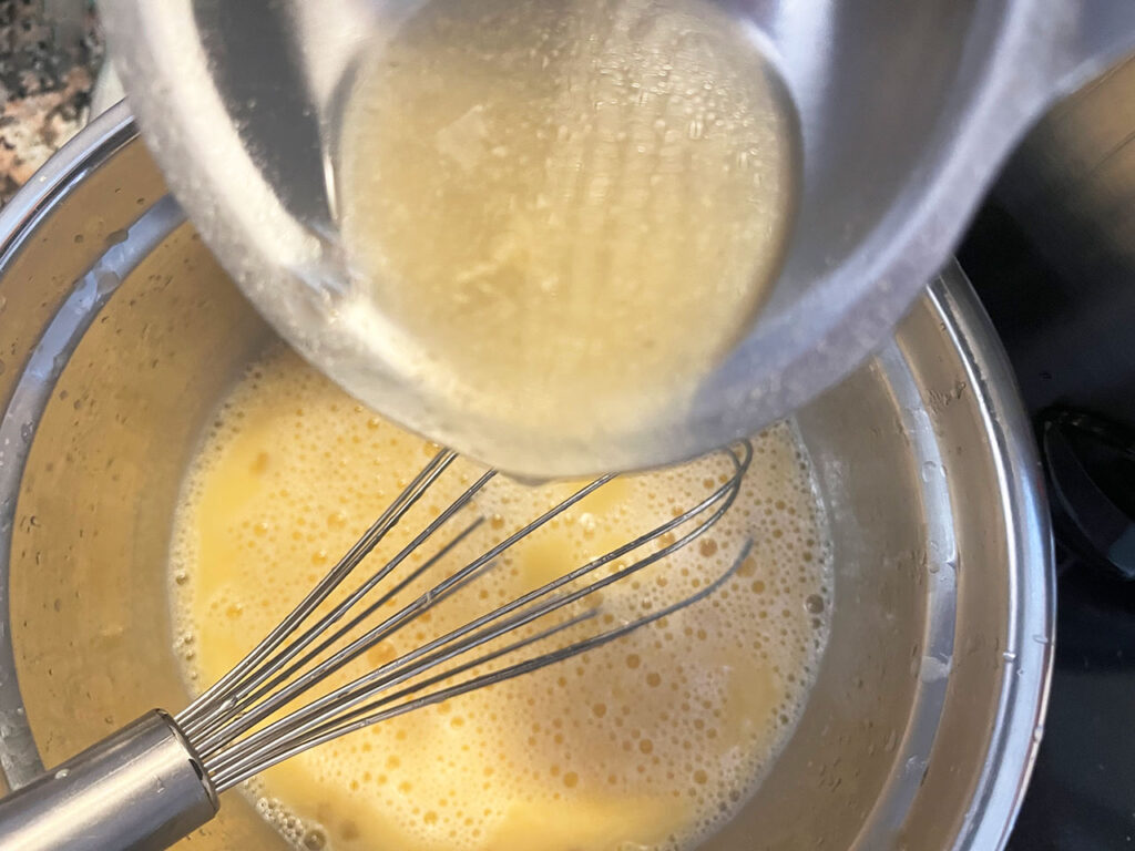 Tempering egg mixture with hot broth. Overhead focus.