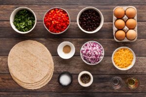Healthy Breakfast Burrito ingredients in bowls on a wood surface.