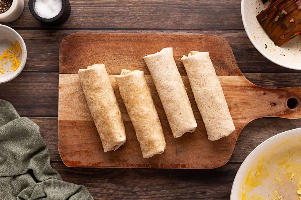 Rolled Healthy Breakfast Burritos on a wood cutting board.