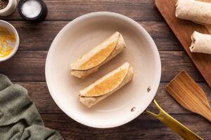 Two Healthy Breakfast Burritos in a skillet with the flap side cooked to keep it in place.