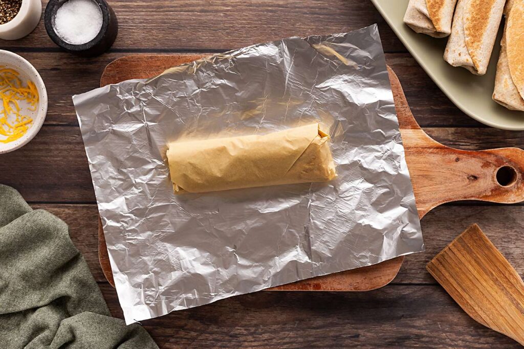 A Healthy Breakfast Burrito wrapped in parchment, laying on a piece of foil.