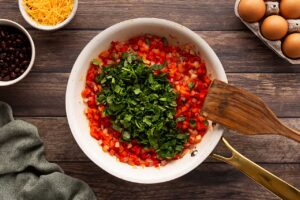 Fresh herbs added to cooked onions and peppers in a skillet.