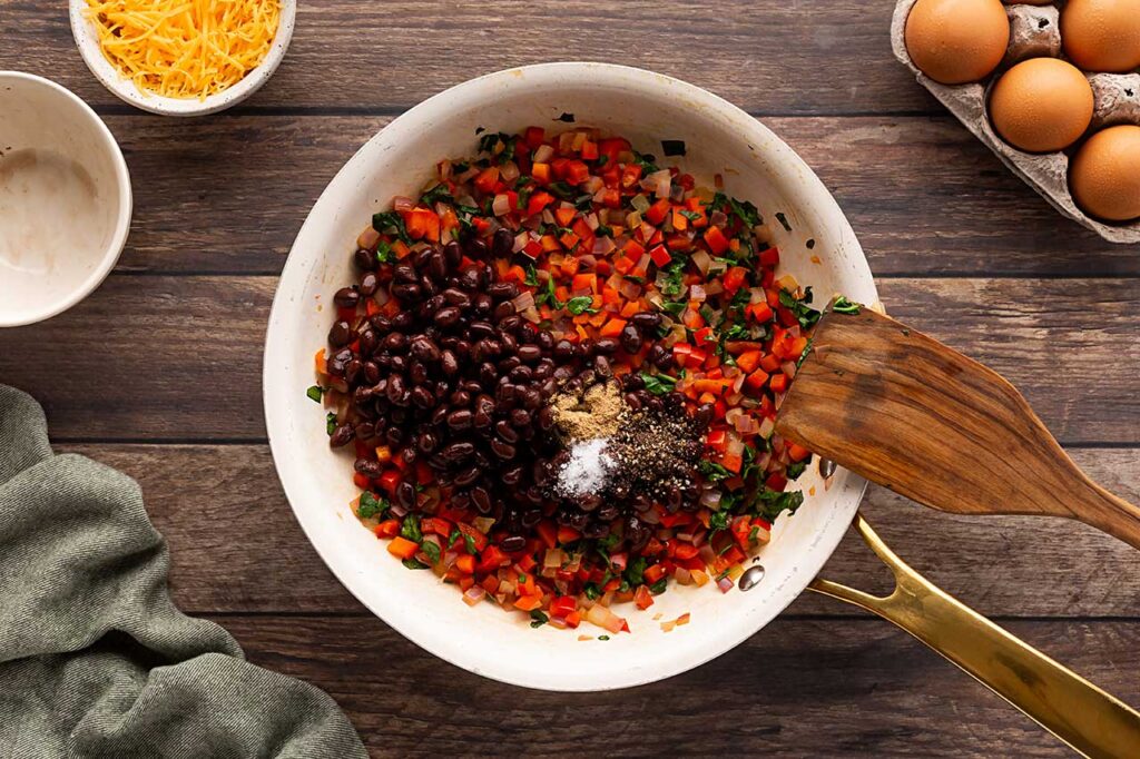 Black beans added to vegetable mix in a skillet.