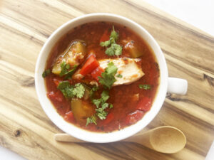 Overhead focus. A white mug on a wood surface filled with Mediterranean Chicken Soup.