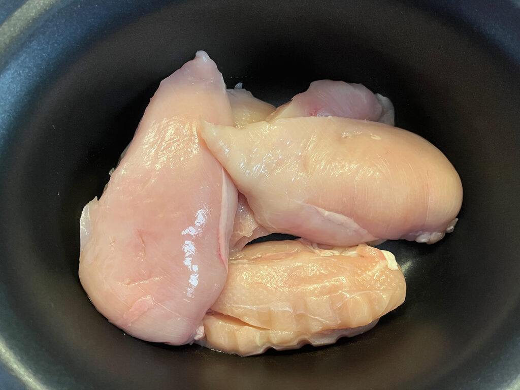 Raw chicken breasts in a slow cooker crock.