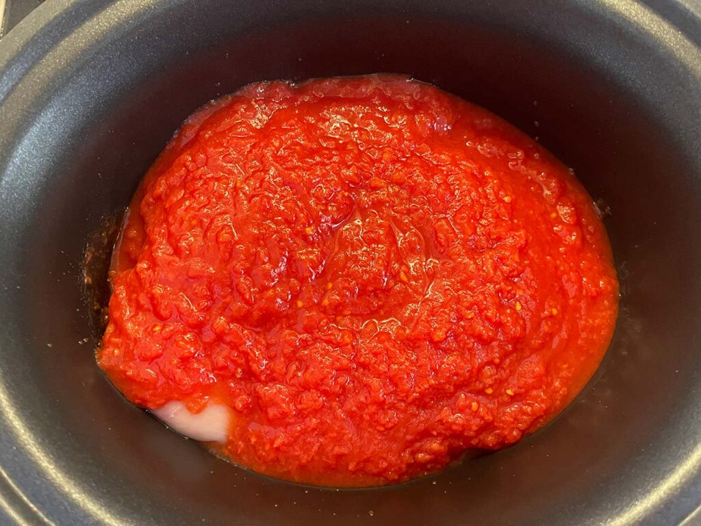 Crushed tomatoes added to a slow cooker crock.