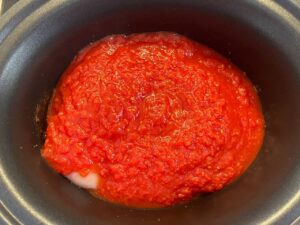 Crushed tomatoes added to a slow cooker crock.