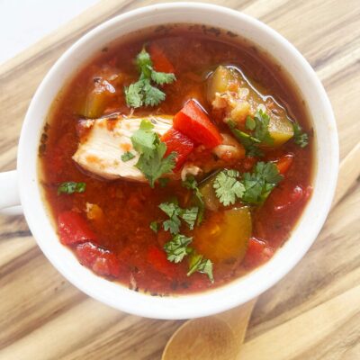 Overhead focus. A white mug filled with Mediterranean Chicken Soup sitting on a wood surface.