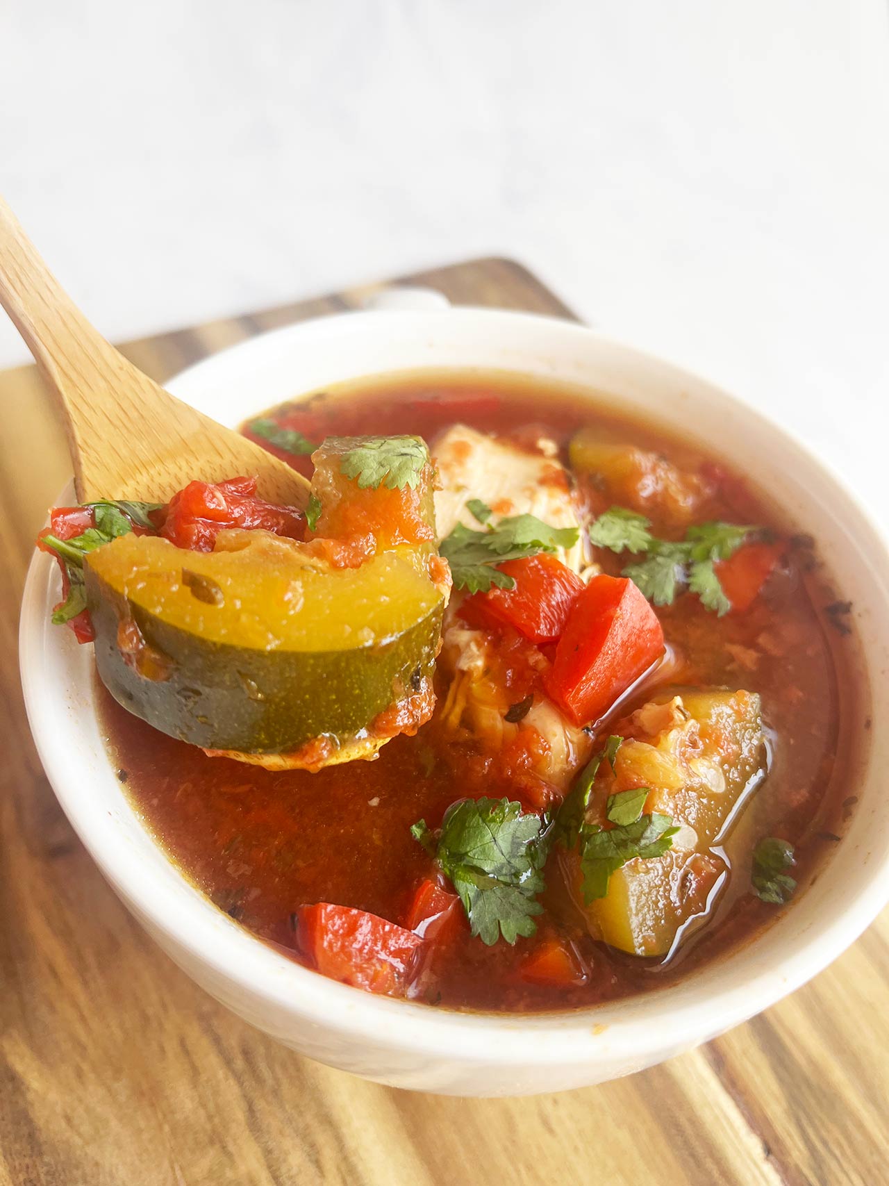 A spoon lifts a bite of Mediterranean Chicken Soup from a mug.