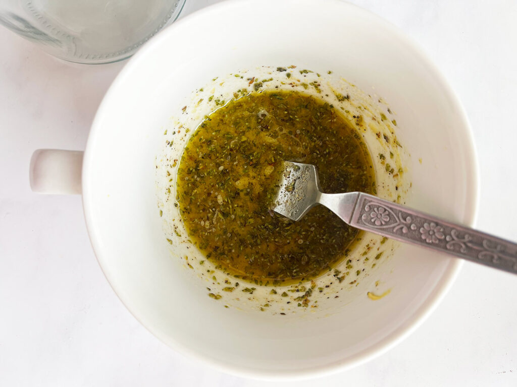 Mediterranean Detox Salad Jars salad dressing mixed in a white mug with a fork.