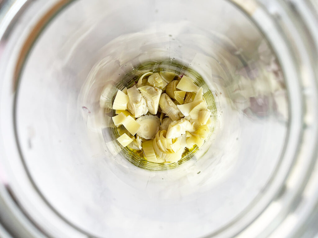 Onions and artichoke hearts added to the bottom of a salad jar.