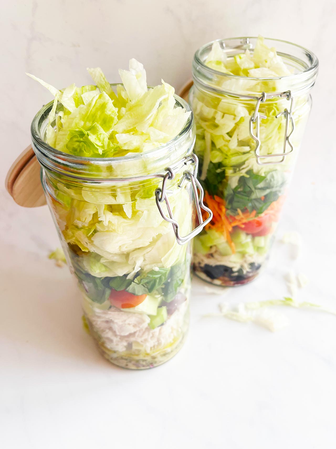 Slightly overhead view of two open Mediterranean Detox Salad Jars on a white background.