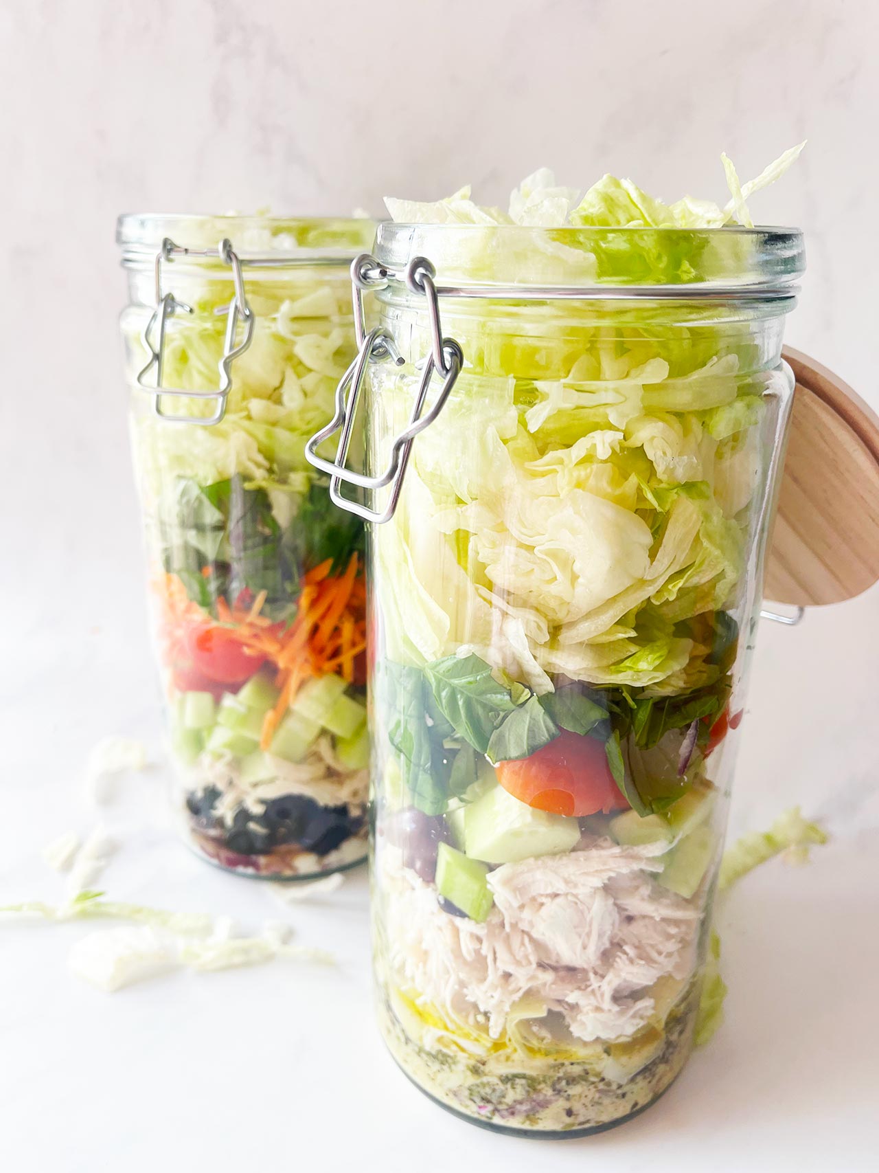 Front view. Two Mediterranean Detox Salad Jars with the lids open, on a white background.