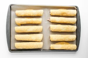 Rolled Chicken Taquitos laid in two rows on a baking pan.