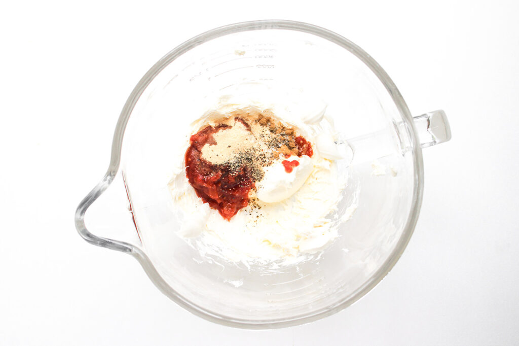Seasonings added to blended cream cheese in a glass mixing bowl.