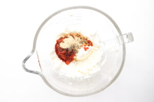 Seasonings added to blended cream cheese in a glass mixing bowl.