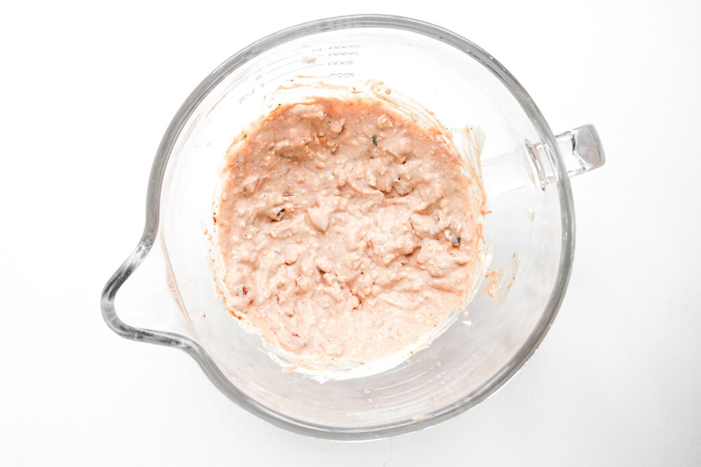 Seasonings blended into cream cheese in a glass mixing bowl.