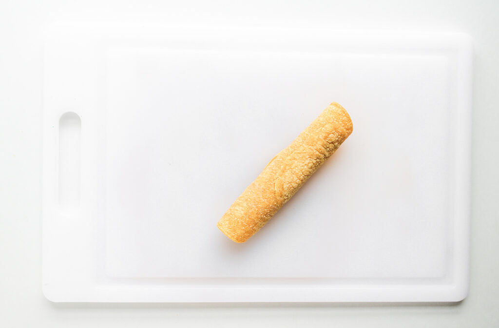 A rolled Chicken Taquito on a white cutting board.