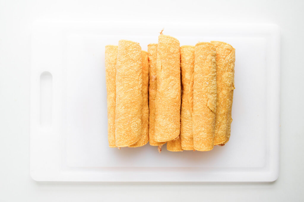 A stack of just-rolled Chicken Taquitos on a white cutting board.