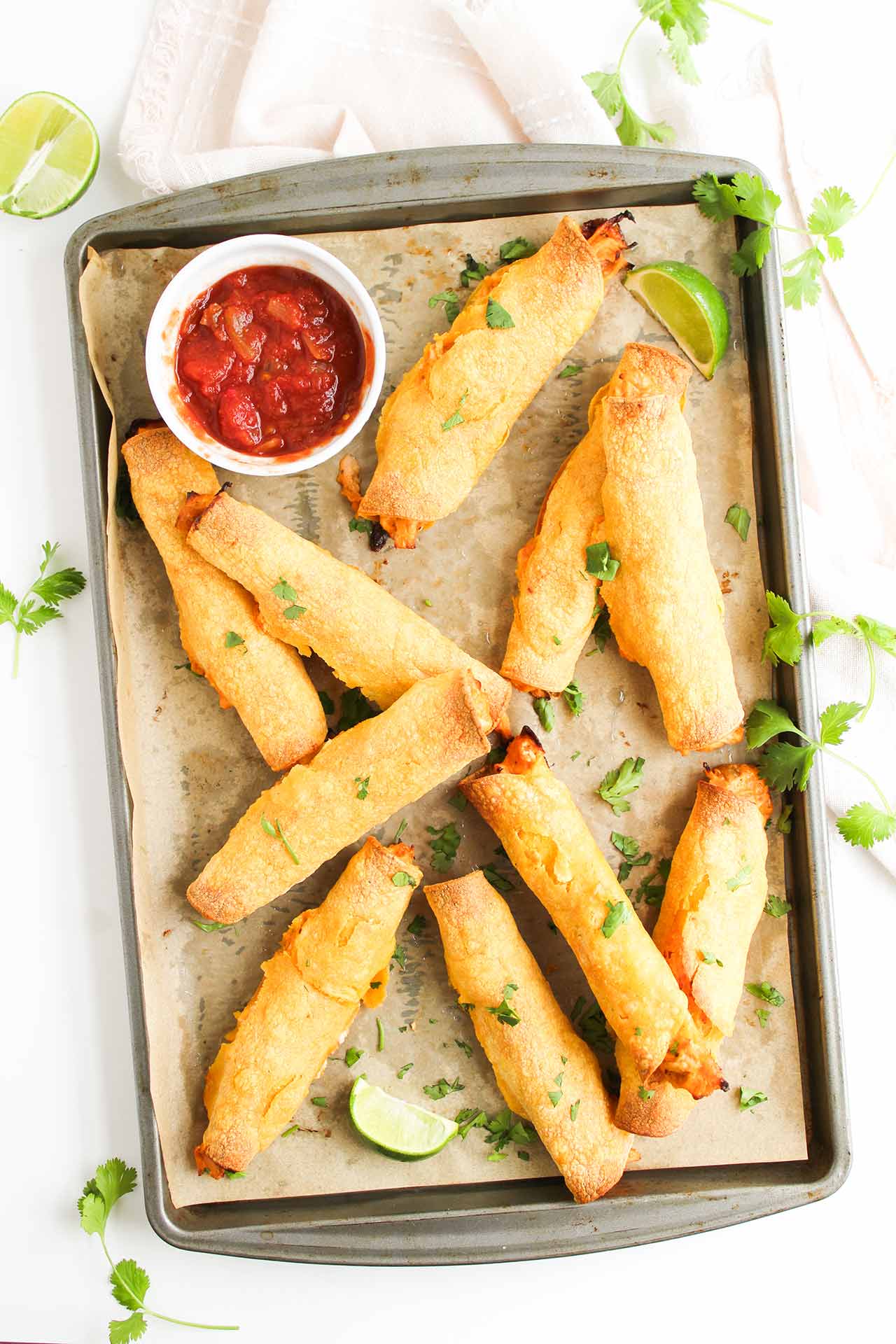 Overhead view of baked chicken taquitos on a parchment-lined baking sheet.
