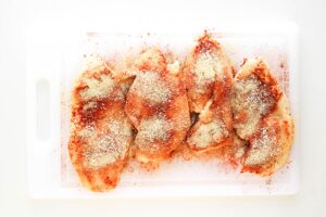 Seasoned chicken breasts on a white cutting board.