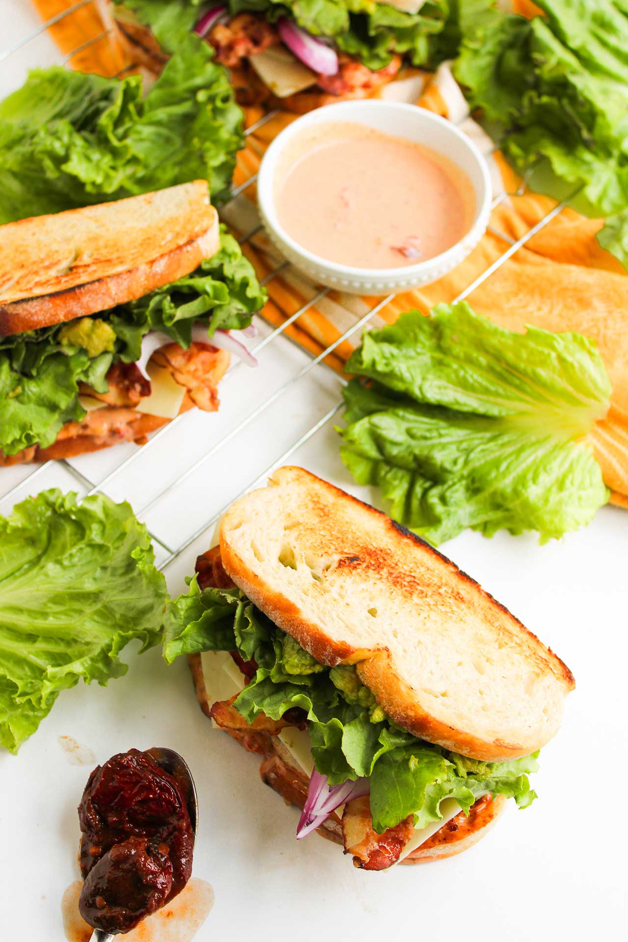 Chipotle Chicken Club Sandwiches on a white surface. A bowl of chipotle sauce sits next to them.