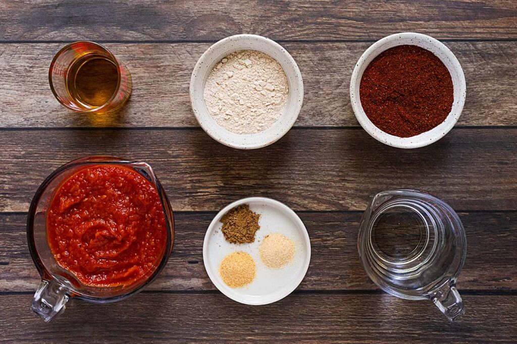 Homemade Enchilada Sauce ingredients in individual bowls on a wood surface. Overhead view.
