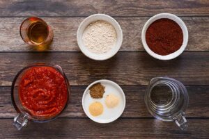 Homemade Enchilada Sauce ingredients in individual bowls on a wood surface. Overhead view.