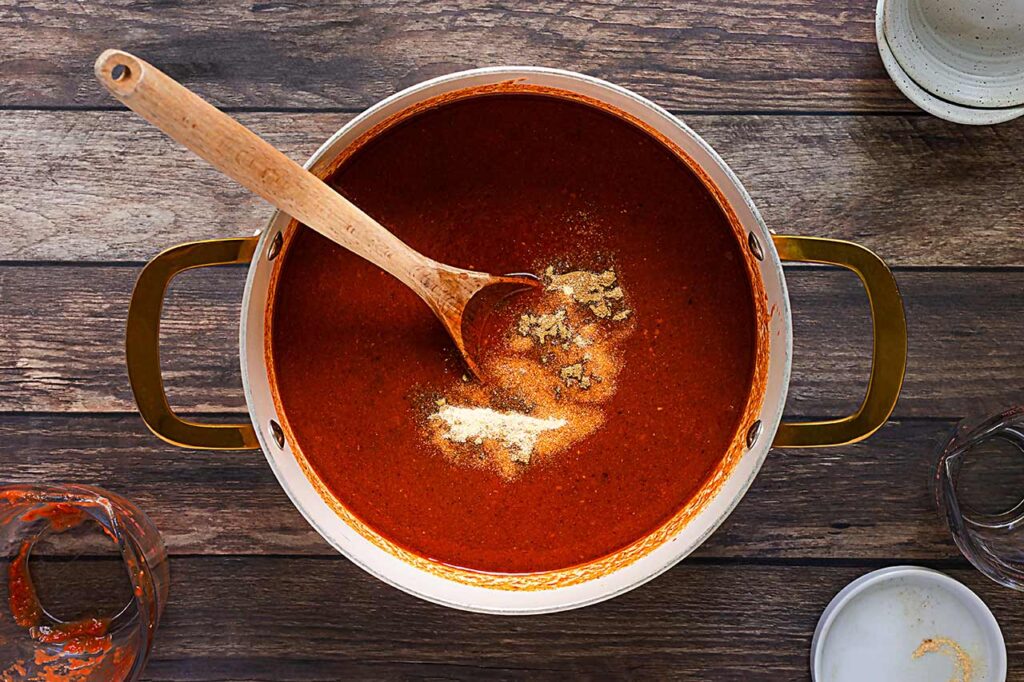 Spices added to Enchilada Sauce in a pot.