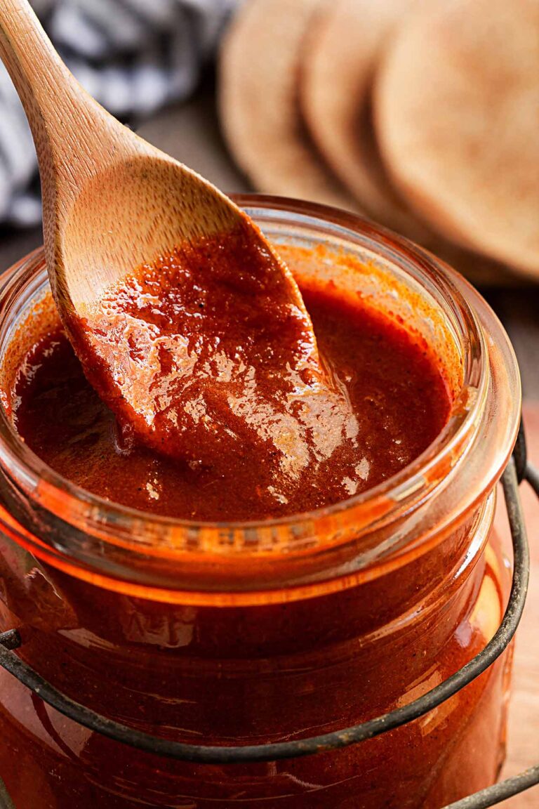 A spoon dips into an open jar of homemade Enchilada Sauce.