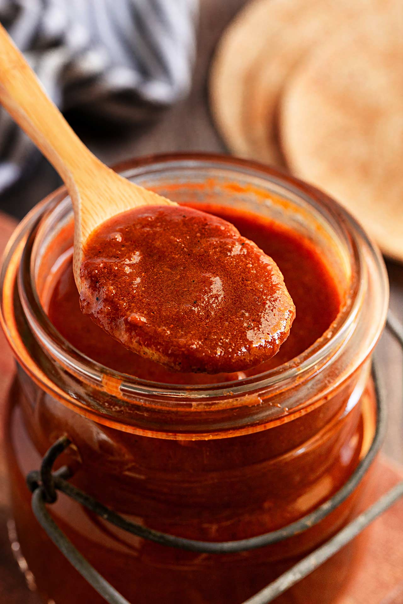 A spoon lifts some Enchilada Sauce from an open canning jar.