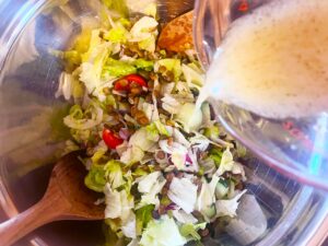 Adding dressing to a Fusion Lentil Salad in a mixing bowl.