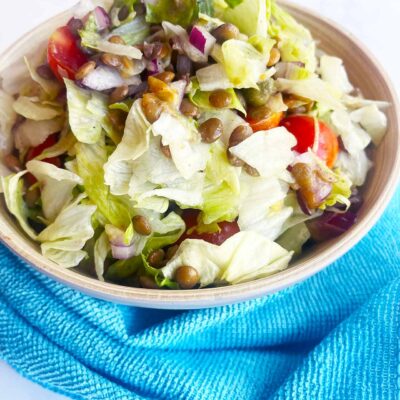 Front view of a bowl of Fusion Lentil Salad with a blue towel in front of it, on a white background.