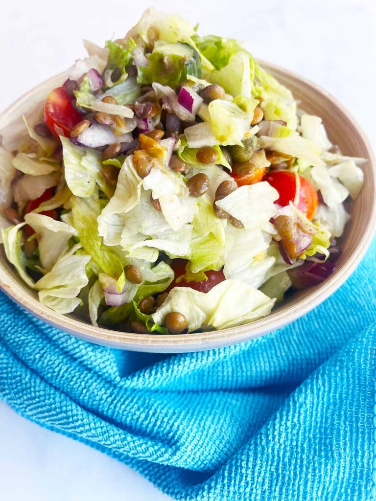 Front view of a bowl of Fusion Lentil Salad with a blue towel in front of it, on a white background.