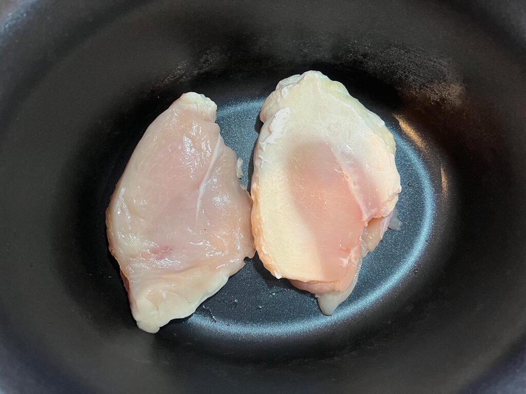 Two chicken breasts in a slow cooker crock.