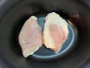 Two chicken breasts in a slow cooker crock.