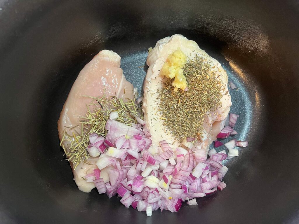 Onions and garlic added to chicken in a crock with herbs.