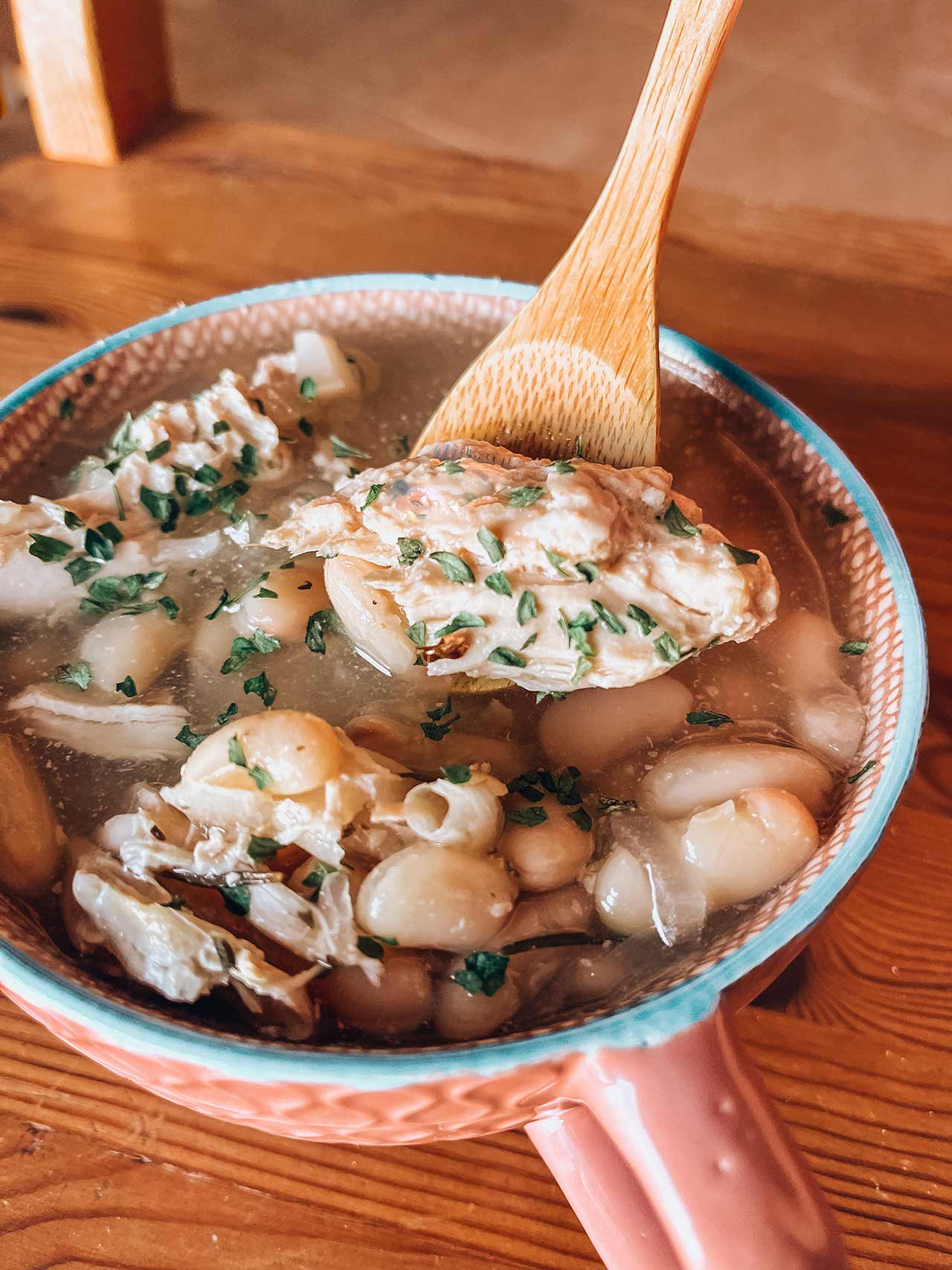 Herb Chicken And White Bean Soup in a mug with a wooden spoon.