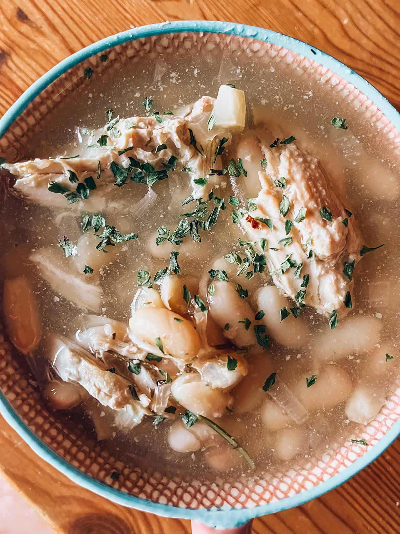 A mug full of Herbed Chicken And White Bean Soup. Overhead view.