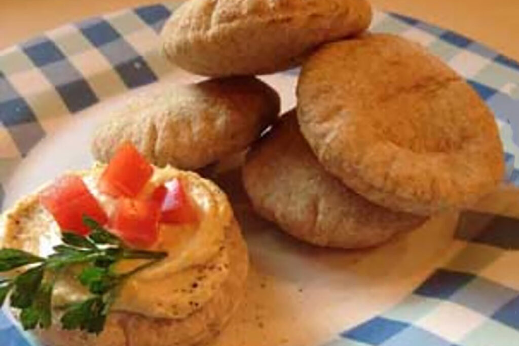 Mini whole grain pita breads with hummus and chopped tomatoes sit on a plate, ready to enjoy.