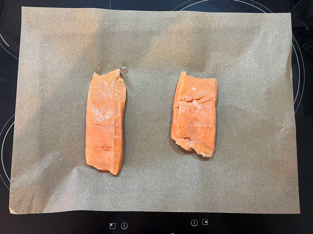 Two raw salmon fillets on a parchment-lined baking sheet.