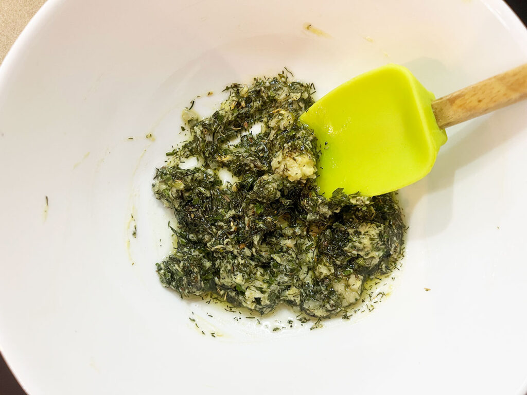 Herb mix in a white mixing bowl with a spatula.